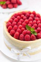 Birthday spongecake with raspberries decorated white ribbon and bow on a white plate