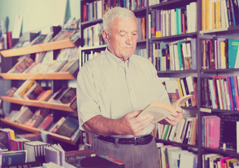 Old male is choosing book for reading in free time in bookstore.