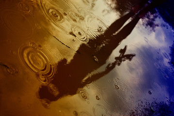 Female silhouette reflected in a puddle in the rain