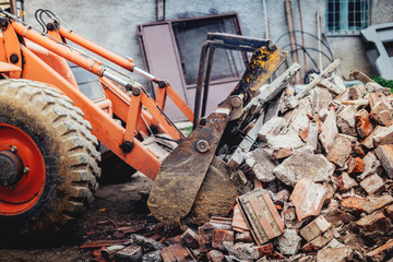 bulldozer demolishing an old building and carrying debris into dumper trucks