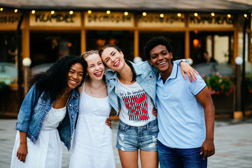 Multiethnic group of four friends hugging and enjoying the summer outdoor in th city street.