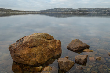 In the fall of seashore with big stones at low tide with reflection of clouds .