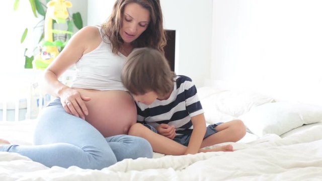Pregnant mother and her son, watching mom's belly and listening to the unborn baby, having fun together