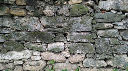 Old masonry of irregularly shaped green mossy stones. Aged stonework