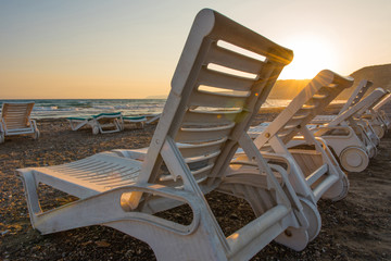 White sunbeds in a sandy beach at sunset