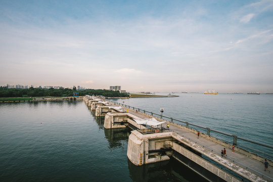 On the dam or top of dyke, people are doing some activities, jogging, running, talking. The dam is also doing its jobs to protect water coming in and out. The sea water is confined by the concrete. 