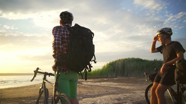 Two young cyclists enjoy the sunset with bikes seaside slow motion rapid 