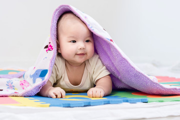 Portrait of a little adorable infant baby girl with blanket lying on the tummy on colorful eva foam indoors