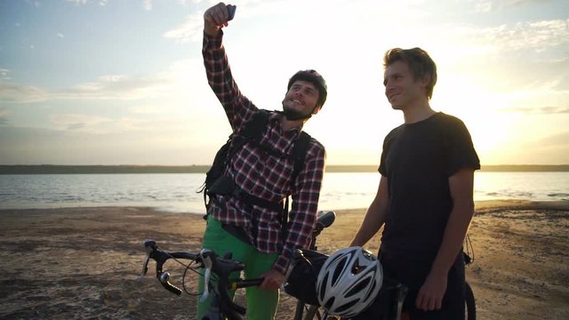 Two young cyclists make selfie on smartphone seaside dawn slow motion rapid 