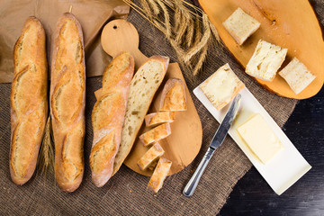 still life with French fresh bread baguettes with poolish on a wooden cutting board, butter and wheat. Shallow dof, flat lay
