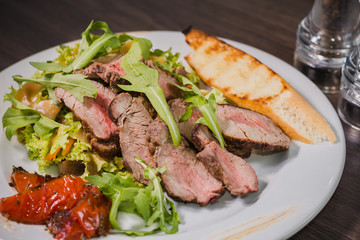 Roasted meat with blood in a cut with vegetables on a wooden background