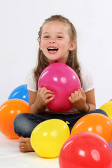 Kleines Mädchen sitzt zwischen Ballons und lacht