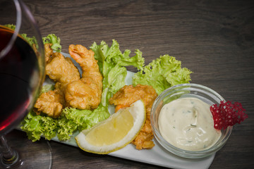 Fried shrimps on a plate with sauce and a glass of wine on a wooden background