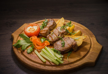 Three pork steaks with fried potatoes and vegetables on a wooden background