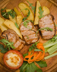 Three pork steaks with fried potatoes and vegetables on a wooden background