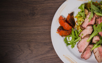 Roasted meat with blood in a cut with vegetables on a wooden background