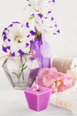 Purple eustoma flowers and lit candle on white table