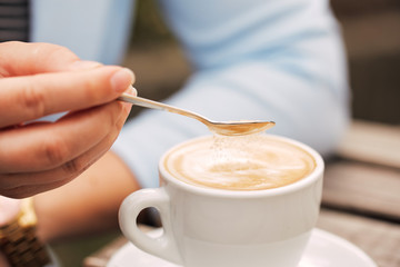 Close-up of a spoon in a female hand pouring sugar into her coffee cup
