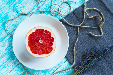 Half of grapefruit on white plate on turquoise wooden table with rustic serving. Healthy food and diet concept. Top view. Flat lay.