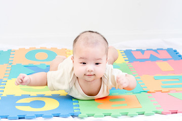 Portrait of a little adorable infant baby girl lying on the tummy on colorful eva foam indoors