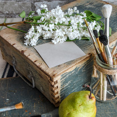 Creative mockup of greeting card and wedding invitation in Shabby chic style. Stylish artist's table with brushes, wooden box, blank, pear, lilac branch.