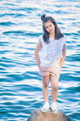 Portrait of little fashionable girl walking on berth near sea