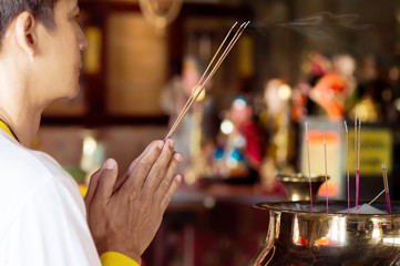 Fototapeta na wymiar Man praying for new year ,lighting incense to Buddha..Burning joss stick and oil palm candle at chinese shrine for making merit in chinese new year festival. .May his life be blessed with health .