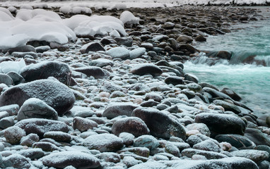 rocks covered in snow flakes on the banks of a turquoise and white river