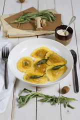 Grilled vegetables ravioli with sage butter. White wooden table, white plate.
