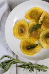 Grilled vegetables ravioli with sage butter. White wooden table, white plate.