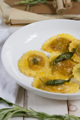 Grilled vegetables ravioli with sage butter. White wooden table, white plate.