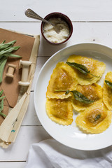 Grilled vegetables ravioli with sage butter. White wooden table, white plate.