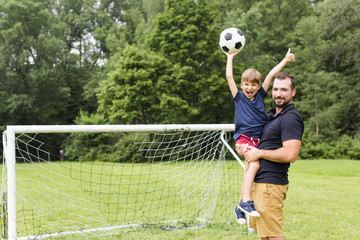 Young father with his little son playing football on football pitch