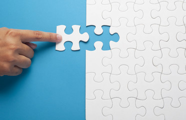 Hand holding piece of white puzzle on blue background. Business and team work concept.