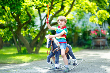 Little kid boy playing with his toy rocking horse in a summer park.