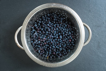 Colander with freshly washed organic blueberries on grey slate stone board.