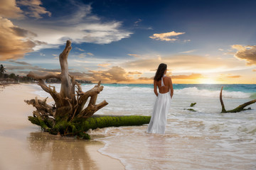 Frau in weißem Kleid steht am Strand in der Karibik bei Sonnenuntergang