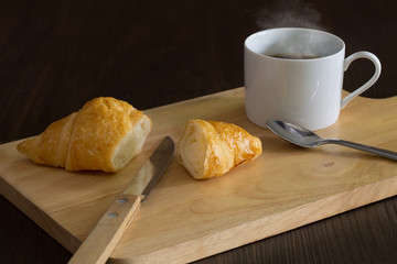 Croissant and black coffee on the chopping wooden board and all on dark background / Selective focus and dim light..