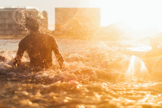 A young man emerges out of the ocean surf at sunset
