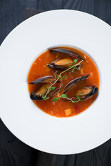 Above view of a white plate with mussels soup, close-up, vertical shot