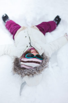 Smiling girl with fur hood making snow angel