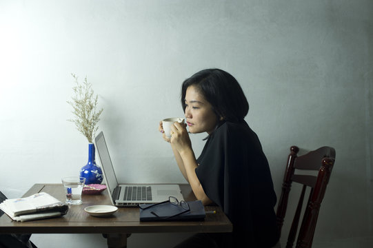 Businesswoman holding a cup of coffee while working on laptop at a cafe