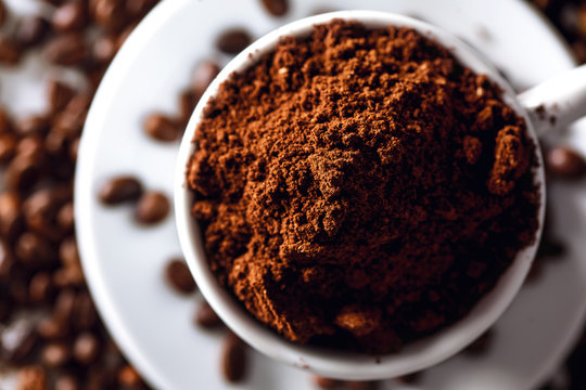 Close up of a coffee cup with coffee grounds and coffee beans around
