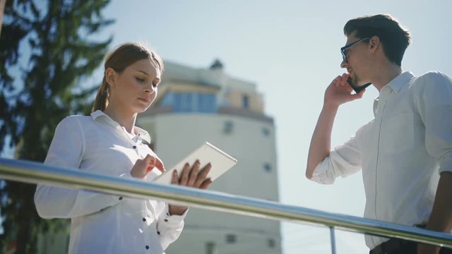 Business man woman tablet computer standing street talking phone using laptop tapping touching screen casual speaking showing display sunny networking young smiling glasses discussing pair work ideas