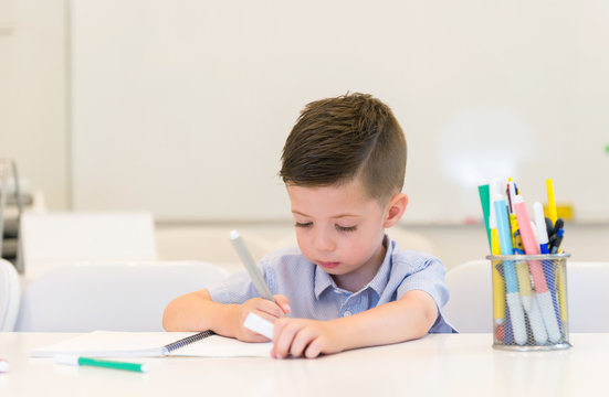 child preschooler boy drawing on booklet ,while sitting on the desk in the classroom