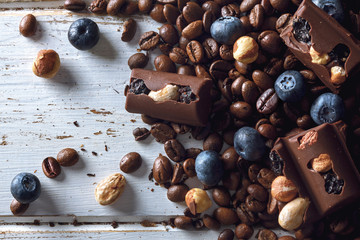 Roasted coffee beans with blueberries, chocolate and hazelnuts over a white wood table