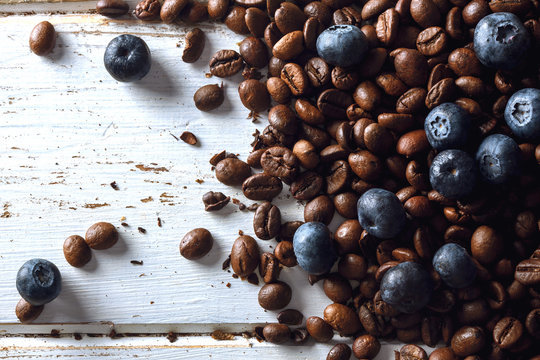 Roasted Coffee Beans With Blueberries Over A White Wood Table