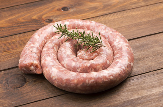 From above raw sausage with rosemary branch on wooden table.