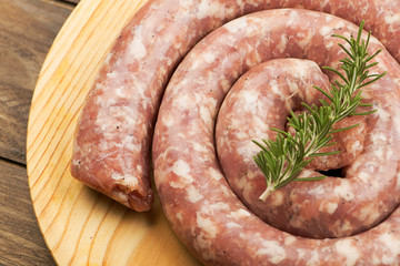 From above raw sausage with rosemary branch on wooden table.