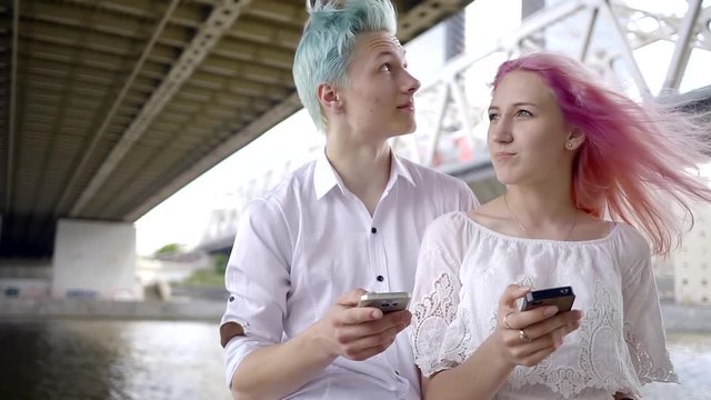 two young people with colorful hair use a mobile when walking in the city. modern technology for Internet. the girl with pink hair and her favorite man with blue hair